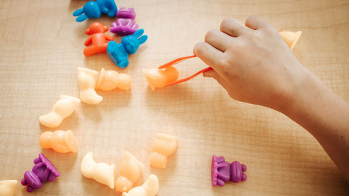 Colorful plastic toys on a wooden surface with a hand interacting with them during occupational therapy session at Excel Therapy Services