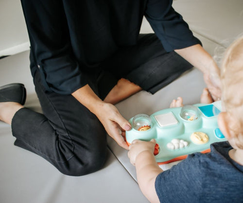 Person and child interacting with a colorful educational toy on a light-colored floor during therapy session.